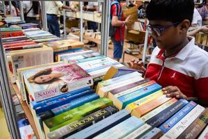 Delhi, India, February 17 2024 - Various age group people reading variety of Books on shelf inside a book-stall at Delhi International Book Fair, Books in Annual Book Fair at Bharat Mandapam complex photo