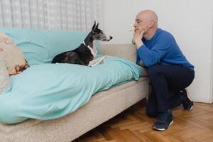 A middle-aged man gives a cookie to his dog with his mouth. photo