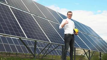 Porträt von ein erfolgreich jung Geschäftsmann auf das Hintergrund von ein Solar- Leistung Bahnhof. Ingenieur prüft Solar- Paneele Produktivität video