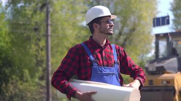 Portrait of a worker in a uniform and a white helmet on the background of special road equipment. Road repair concept video