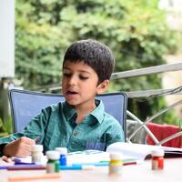 inteligente indio pequeño chico realizar pulgar pintura con diferente vistoso agua color equipo durante el verano vacaciones, linda indio niño haciendo vistoso pulgar pintura dibujo en de madera mesa foto