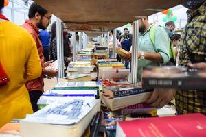 Delhi, India, February 17 2024 - Various age group people reading variety of Books on shelf inside a book-stall at Delhi International Book Fair, Books in Annual Book Fair at Bharat Mandapam complex photo