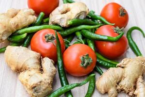 Fresh Ginger, Tomato and green chili pepper on plain wooden table, green essential vegetables for all essential foods, view of unpeeled vegetables with plain background photo