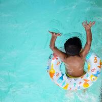 Happy Indian boy swimming in a pool, Kid wearing swimming costume along with air tube during hot summer vacations, Children boy in big swimming pool. photo