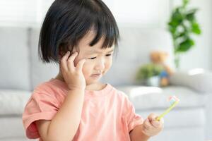 little asian girl presses hand to cheek, suffers from pain in tooth. Teeth decay, dental problems, child emotions and facial expression, oral health care, reducing sweets, fluorine coating photo