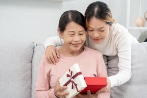 madre día, linda asiático adolescente niña dar regalo caja a maduro medio años mamá. amar, beso, cuidado, contento sonrisa disfrutar familia tiempo. celebrando especial ocasión, contento cumpleaños, contento nuevo años, alegre Navidad foto