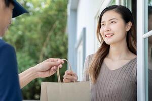 Happy smiling Asian woman receives paper bag parcel of food from courier front house. Delivery man send deliver express. online shopping, paper container, takeaway, postman, delivery service, packages photo