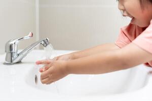 pequeño niño manos lavar con jabón burbujas y enjuague con limpiar agua a evitar y detener el untado de gérmenes después espalda a hogar, virus o COVID-19. bueno salud y bueno personal higiene, virus, bacterias foto