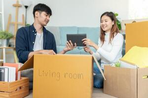 Moviente casa, reubicación Pareja ayuda conjunto y moverse mueble para nuevo departamento, dentro el habitación estaba un cartulina caja Contiene personal pertenencias. moverse en el nuevo Departamento o condominio foto