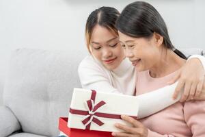 madre día, linda asiático adolescente niña dar regalo caja a maduro medio años mamá. amar, beso, cuidado, contento sonrisa disfrutar familia tiempo. celebrando especial ocasión, contento cumpleaños, contento nuevo años, alegre Navidad foto