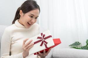 una mujer bastante asiática se siente sorprendida y mira interesada dentro de la caja de regalos. linda chica emocionada caja de regalo abierta. cumpleaños, celebración, navidad, festival de año nuevo, gracias, celebrar, día de san valentín, aniversario foto