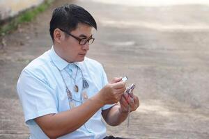 Asian man hold small magnifying glass to inspect detail and pattern of amulet. Concept, faith and belief in holy and luck for Buddhists. Colleting amulet as hobby, exchange or trade. Culture of faith. photo