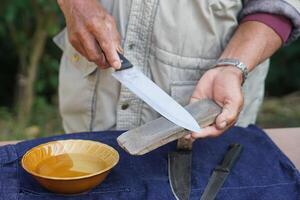 Closeup man hands sharpen knife on whetstone sharpener or grindstone. Concept, maintenance tools for cooking, make knife sharp ,not dull for long live using. Original style. photo