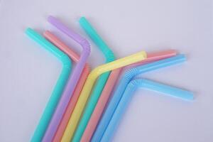 Colorful plastic drinking straws tubes for juice and cocktails, gray background. Concept, single use equipment for drinking, but can use for diy crafts for decoration. photo