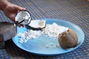 Hands holding a half-cut coconut to scrape for making coconut milk by using coconut grater. Concept Thai cooking style. Food ingredient in traditional food and dessert. photo