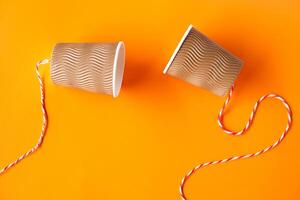 Two paper cups tied with rope for making telephone toy. Orange background. Concept, telephone toys which apply with science knowledge about vibration sound through straining strings causing us to hear photo