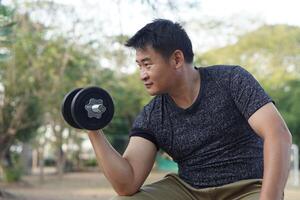 Handsome Asian man exercises outdoor, lift dumbbell. Concept, Exercise for health bodybuilding. Strengthen muscle. Weight lifting. Healthy lifestyle. Sport equipment. Work out makes strong of body. photo