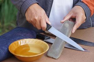 Closeup man hands sharpen knife on whetstone sharpener or grindstone. Concept, maintenance tools for cooking, make knife sharp ,not dull for long live using. Original style. photo