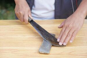 Closeup man hands sharpen knife on whetstone sharpener or grindstone. Concept, maintenance tools for cooking, make knife sharp ,not dull for long live using. Original style. photo