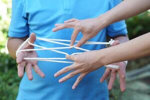 Close up two men playing with rope traditional game called cat cradle, use hands to hold  and create patterns of rope . Concept, game involving the creation of various style figures between fingers photo