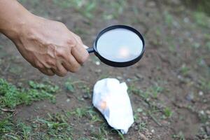 cerca arriba mano sostener aumentador vaso a hacer fuego para ardiente papel. concepto, Ciencias experimentar acerca de convexo lente, sostener aumentador vaso Entre el Dom y Tinder. práctico supervivencia habilidades. foto