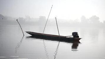 gammal trä- båt på vatten av morgon- flod i magi soluppgång Sol ljus, dimma på de sjö på soluppgång tid, båt förtöjd till de Bank av en damm, fiske båt video