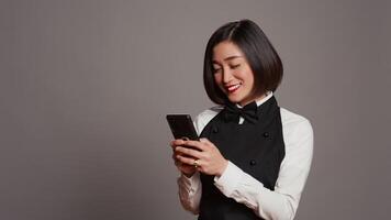 Restaurant Hostess SMS Mitteilungen zu bestätigen Reservierungen auf Telefon Anwendung, Arbeiten im Gastronomie und Portion Industrie. asiatisch Kellnerin mit Smartphone online Webseiten, Sozial Medien. Kamera b. video