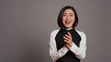 Restaurant hostess clapping hands and celebrating for someone, cheering and saying congratulations in studio. Asian waitress with uniform and apron applauding a person, acclaim. Camera B. video