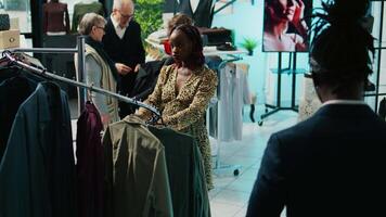 African american pregnant client checks t shirts on hangers, looking to buy more comfortable pregnancy clothing items. Woman customer examining colorful clothes on display. Camera B. video