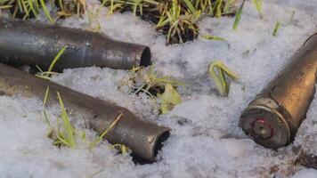 Macro time-lapse shot of shiny melting snow particles turning into liquid water and unveiling green grass and machine gun ammo. The concept of the past war. video