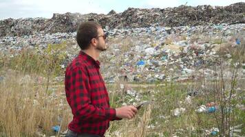 Garbage dump inspector with tablet records pollution level on city dump video