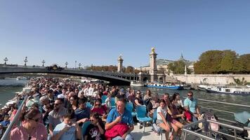 Paris, France 29.09.2023 Tourists Enjoying Seine River Cruise Crowded tourist boat on the Seine River passing under a historic bridge with the iconic architecture of Paris in the background. video