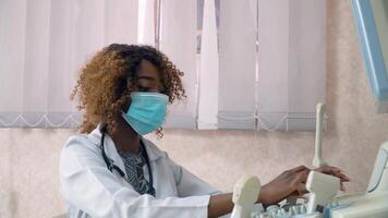 African american woman doctor in protective mask examines patient in ultrasound device monitor. Coronavirus diagnosis video