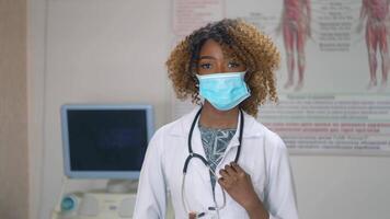 Portrait of professional african american female doctor in medical mask. Hospital with ultrasound devices on background. Stop virus video