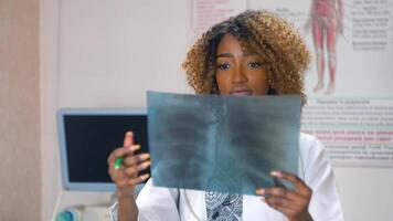 Female african-american doctor examines x-ray of lungs in clinic. Doctor examines x-ray of lungs of a patient with coronavirus video