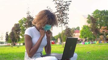 jovem africano americano fêmea aluna colocando em protetora mascarar e trabalhando em computador portátil dentro parque video