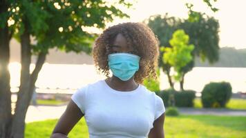 afrikansk amerikan flicka i medicinsk mask ser på de kamera i parkera video