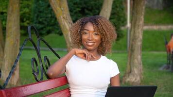 lindo jovem africano americano mulher bonita face com computador portátil olhando às Câmera posando sozinho dentro uma universidade parque, feliz milenar africano etnia menina aluna profissional fechar acima frente retrato video