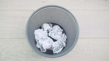 Throw crumpled into the trash. Overflowing waste paper in office garbage bin. Junk, wastepaper in rubbish isolated on wooden background video