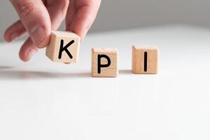 Close up young man's hand in white shirt wooden block cube for Kpi wording on white marble table floor photo