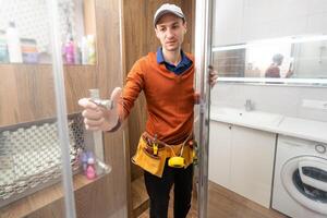 young foreman measuring shower cabin in modern bathroom. photo