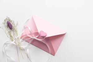 Minimal composition with a pink envelope, white blank card and a wax flower on a white background. Mockup with envelope and blank card. Flat lay. Top view. photo