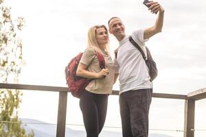 A man and a woman in tourist equipment are standing on a rock and admiring the panoramic view. A couple in love on a rock admires the beautiful views. A couple in love is traveling. A couple on a hike photo