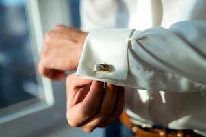 elegante joven hombre consiguiendo Listo para boda. cerca arriba de mano hombre vistiendo blanco camisa y gemelo foto