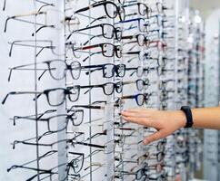 Row of glasses at an opticians. Eyeglasses shop. Stand with glasses in the store of optics. Woman's hand showes glasses. Presenting spectacles. photo