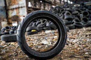 Old car wheel stand on the dirty ground on the bunch of tires background. Rubber used tire from automobile. Close-up photo