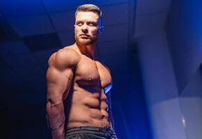 Strong athletic man fitness model torso showing six pack abs. isolated on dark background with blue filter. Closeup. photo