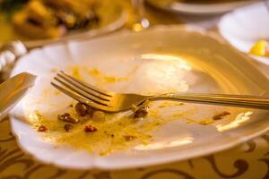 sobras y tenedor en blanco lámina. sucio vacío plato con tenedor en un mesa en restaurante después cena. foto