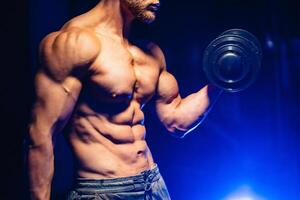 Young handsome sportsman bodybuilder weightlifter with an ideal body, with naked torso poses in front of the camera, abdominal muscles, biceps triceps. Closeup photo