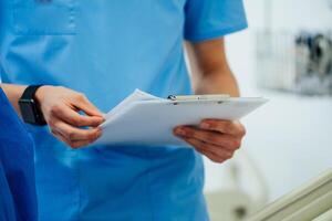 Doctor in blue scrubs holding medical records and prescriptions in the operating room. Closeup photo